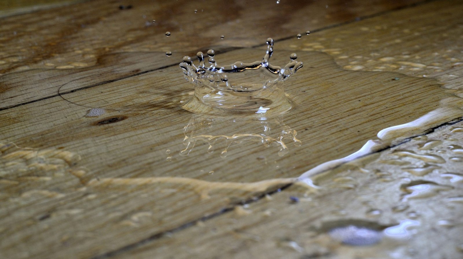 Water splashes into a puddle on wooden floorboards.